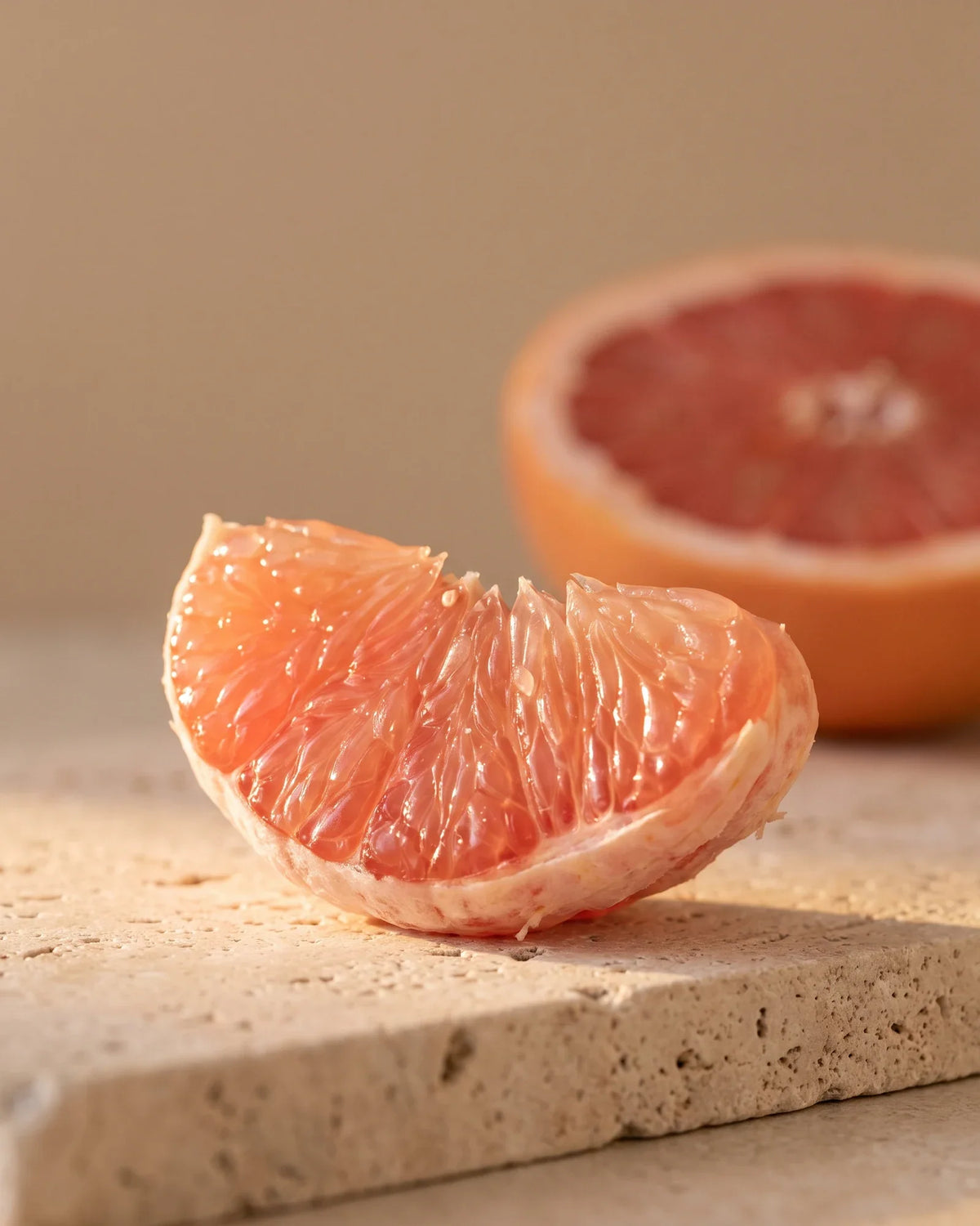 A glistening pink grapefruit segment backlit by warm sunlight — the bittersweet, juicy scent of Delune Grapefruit (Pink) Pure Essential Oil