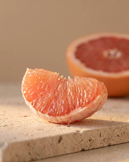 A glistening pink grapefruit segment backlit by warm sunlight — the bittersweet, juicy scent of Delune Grapefruit (Pink) Pure Essential Oil